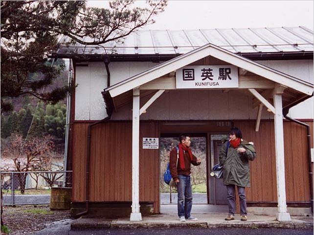 兩人並肩站在車站前，沉默無語。冷清的車站，簡陋得像是臨時搭建的場景。